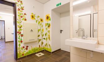 A modern bathroom with a flourishing wall design of sunflowers. There is a sink and a hand dryer in a bright, inviting space.