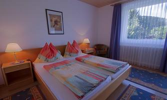 A cozy bedroom with two beds and colorful blankets. Large windows let in plenty of daylight.