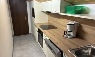 A modern kitchen with bright cabinets and a wooden countertop. Included are a stove, a coffee machine, and a sink.