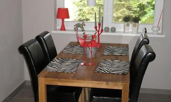 A stylish dining area with a wooden table and black-and-white striped placemats. The surroundings are designed in a modern style and have large windows overlooking greenery.