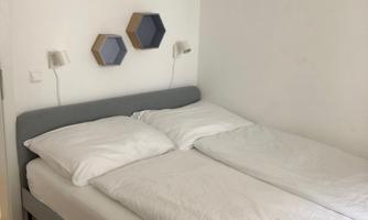 A cozy bedroom with a double bed and modern wall decorations. The walls are light and the furniture is simple and functional.