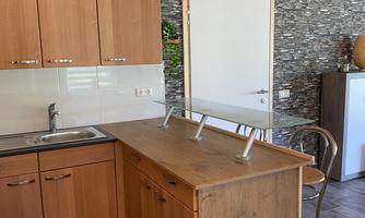 A modern kitchen with wooden cabinets and an open kitchen island. The wall is adorned with stone tiles, and there is a light wooden floor.
