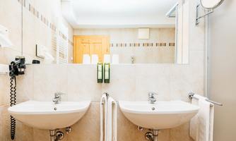 A modern bathroom with two sinks and bright tiles. Towels hang on the wall and toiletries are placed.