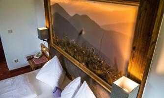 A cozy room with two beds and pillows. On the wall hangs a picture of a mountain landscape at sunset.