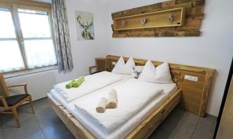 A cozy bedroom with a large wooden bed and two separate mattresses. The walls are light and a small seating area is visible in the background.