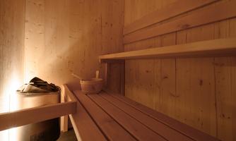 A cozy interior of a sauna with wooden shelves and soft lighting. On a bench, there is a wooden bowl and a towel.