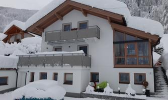 A snow-white house with a balcony and large windows. The front area is completely covered in snow.