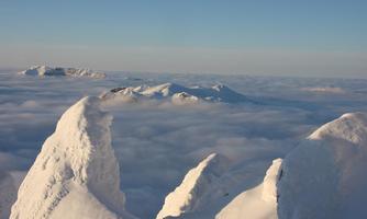 An impressive mountain landscape with snow-capped peaks rising above a blanket of clouds. The sky is clear and a calm, peaceful atmosphere can be felt.