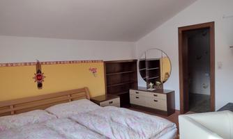 A cozy bedroom with a double bed and colorful bedding. The walls are painted in warm colors and there is a large mirror as well as a wardrobe.