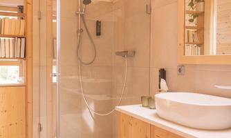A modern bathroom with a rain shower and bright wood surfaces. The sink is elegant, and there is plenty of storage space for towels.