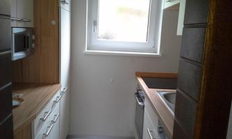 A modern kitchen with white cabinets and wooden details. The room is bright and has a window that lets in daylight.