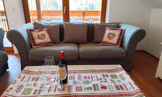 A cozy living room with a gray sofa and decorative cushions. On the table are glasses and a bottle of wine next to a festive table runner.