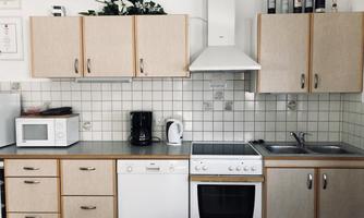 A modern kitchen with light wood cabinets and white appliances. It is well equipped with a stove, a sink, and a microwave oven.
