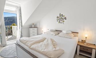 A cozy bedroom with a large bed and a beautiful view of the mountains. The room has bright walls and a balcony with access to nature.