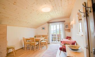 A cozy living space with wood ceilings and a table. The room has large windows with access to a balcony.