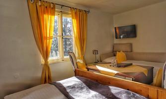 A cozy room with a bed and a dining table. Large windows with yellow curtains let in plenty of light.