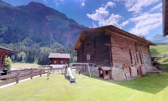 A traditional wooden house in a picturesque, hilly landscape. In the background, mountains and a blue sky can be seen.