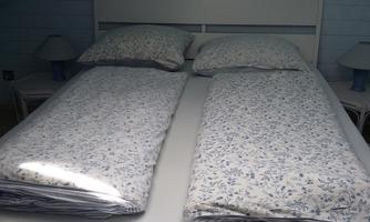 A bedroom with a double bed that has two separate comforters. Next to the bed, there are two nightstands with lamps.