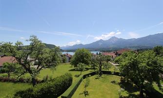 A green landscape with trees and well-maintained gardens. In the background, mountains and a clear sky can be seen.