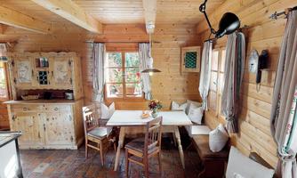 A cozy wooden room with a dining table and chairs. Large windows let in plenty of daylight, and the interior exudes a warm atmosphere.