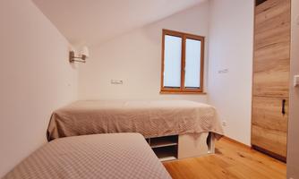 A simple room with two beds and a window. The walls are white and the floor is made of wood.
