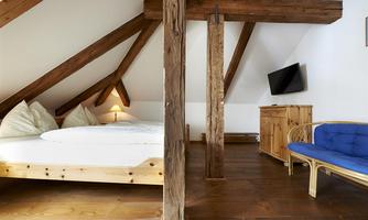 A cozy room in the attic with wooden ceilings and a large bed. The furnishings include a TV and a chair in a quiet setting.