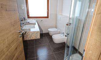 A modern bathroom with a shower and a sink. It has bright walls, a large mirror, and a view from the window.
