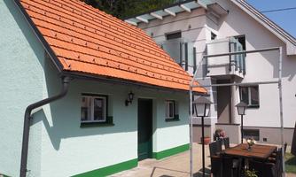 A beautiful building with two houses, one with a green-blue facade and red roof. In front, there is a table with chairs in a cozy garden.