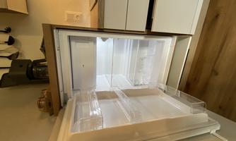 An open refrigerator with an empty interior and clear lighting. The surroundings show a modern kitchen with wooden shelves.