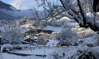 A snowy landscape with snow-covered hills and houses. The trees are covered in snow and the sky is clear.