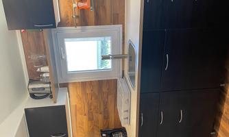 A modern kitchen with black cabinets and wooden cladding. The view from the window shows a green landscape.
