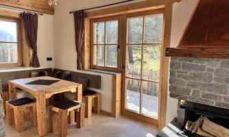 A cozy dining area with a wooden table and chairs. Large windows provide a view of the surrounding nature.