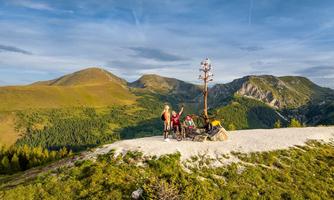 A group of people is standing on a green hill with mountains in the background. The sun is shining and it is a beautiful, clear landscape.