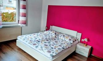 A cozy bedroom with a large bed and colorful bed sheets. The wall behind the bed is painted in a vivid pink.