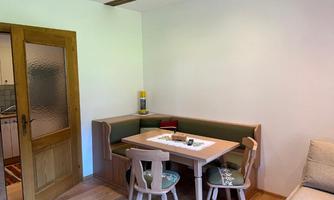 A cozy dining area with a table and chairs, surrounded by a bench. The walls are bright and the furniture is made of wood, creating an inviting atmosphere.