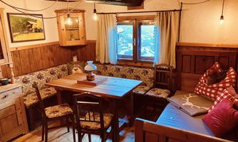 A cozy room with a wooden table, chairs, and a bench. The walls are made of wood and there is a beautiful view through the window.
