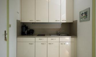 A modern kitchen with bright, shiny furniture. It contains a sink, cooktops, and a coffee machine.