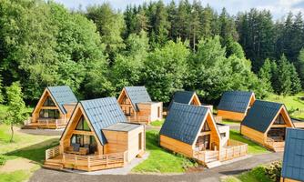 Six modern wooden chalets are situated in a green environment. The buildings feature distinctive, pointed roofs and a cozy atmosphere.