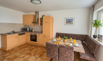 A bright kitchen with wooden cabinets and modern appliances. The dining table is set with breakfast and a plant on the windowsill.