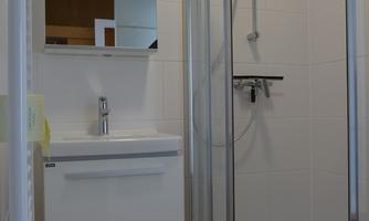 A modern bathroom with a shower cabin and a sink. Bright tiles and a mirror complete the space.