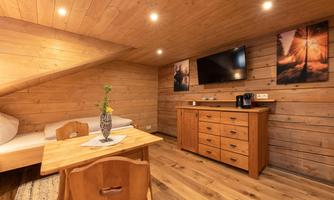 A cozy room with wood paneling, a table, and a small seating area. A television hangs on the wall, and there are decorative pictures.