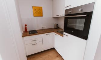 A modern kitchen with white cabinets, wooden countertop, and a built-in oven. A yellow sign with a saying hangs on the wall.