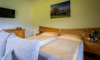 A cozy bedroom with two single beds and a bright, inviting atmosphere. A picture of a landscape hangs on the wall, and a television is also available.