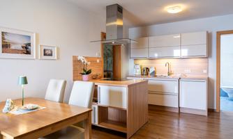 A modern kitchen with a dining area. The space is designed to be bright and friendly, with wood and white tones.