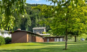 A modern building in a large, green garden.  
Surrounded by trees and hills, the scene radiates tranquility and a connection to nature.