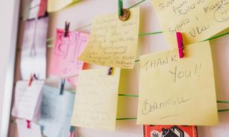 A wall shelf with colorful sticky notes containing various messages and reminders. The notes are attached to a thread with clips.