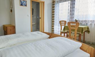 A bright room with two single beds and a table. Large windows provide plenty of daylight.