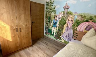 A cozy bedroom with wooden furniture and a colorful wall mural. The room is brightly lit and has a modern lampshade.