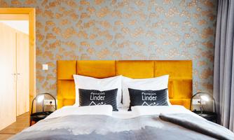 An elegant bedroom with a large double bed and decorative pillows. The walls are designed with a modern pattern in warm tones.