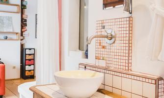 A modern bathroom with a wooden table and a round washbasin. The walls are designed with white and red patterned tiles.